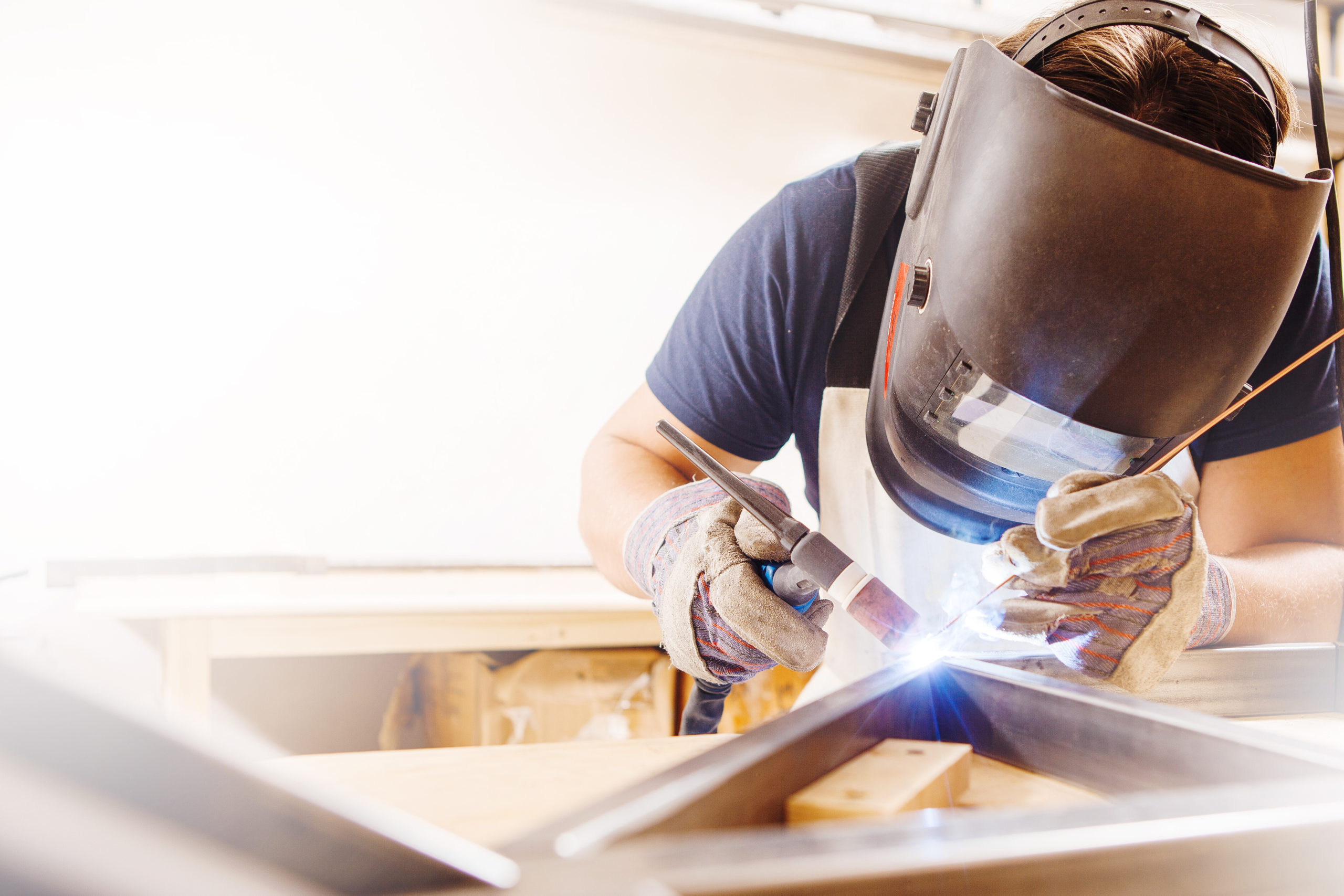 Male in face mask welds with argon-arc welding